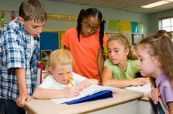 Children standing around one child watching her write