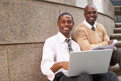 2 African-American men sitting outside with a laptop