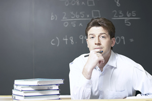 Male teacher sitting at desk and looking up at class